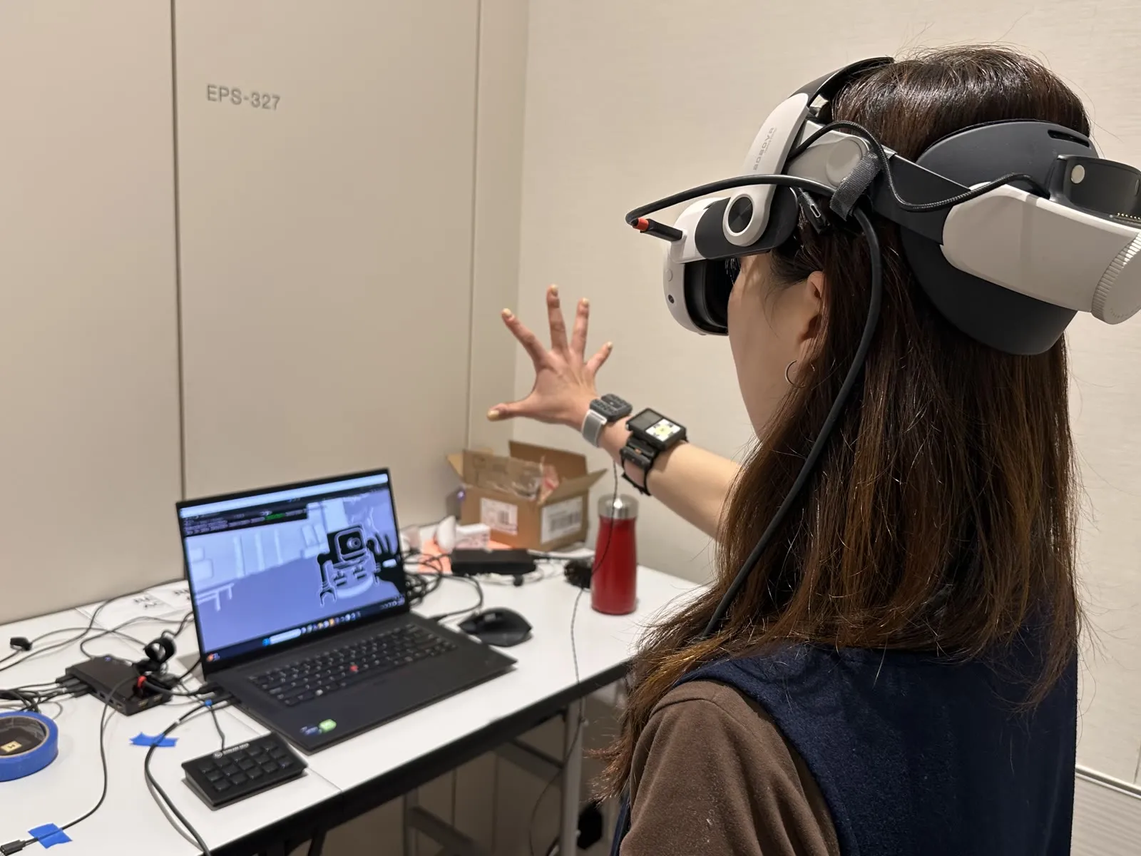 A conference attendee wearing a VR headset and wrist-worn haptic device tries the EMG and haptics demo, with the game visible on a laptop beside them