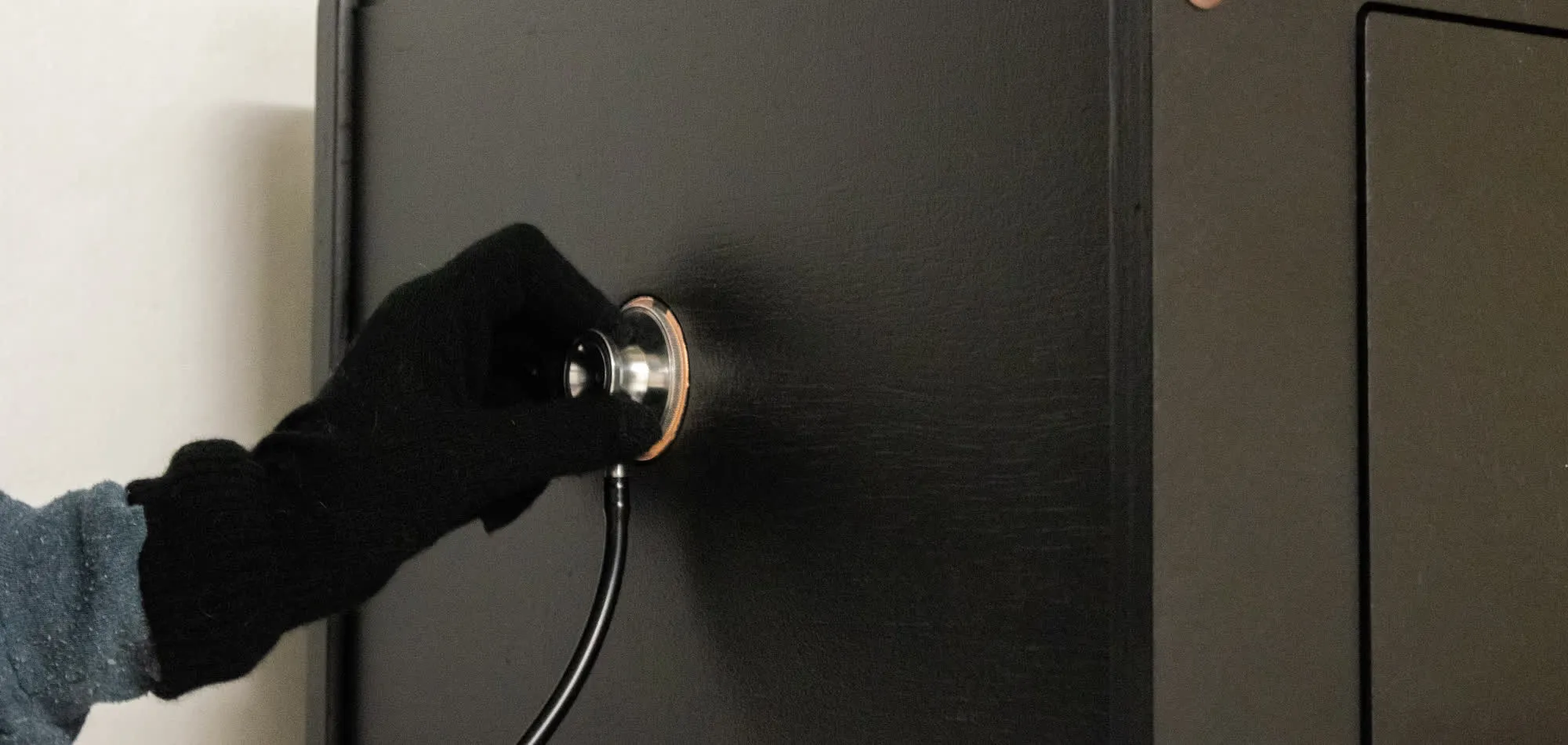 A gloved hand pressing a stethoscope against a copper touch point on the finished safe